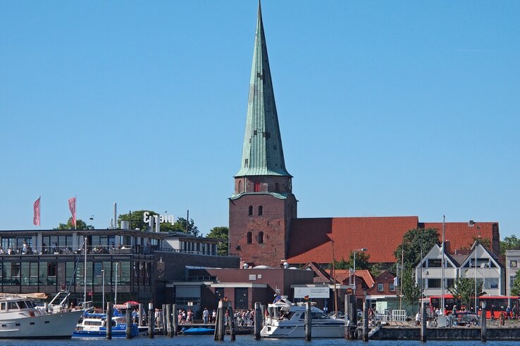 Hafenansicht mit Segelbooten, historischer Kirche und modernen Gebäuden bei klarem Himmel in Travemünde.