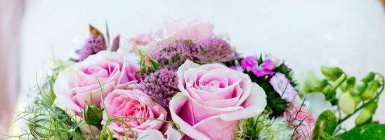 Bride holding a lush bouquet of pink roses with green accents against a blurred green background.