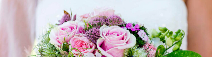 Bride holding a lush bouquet of pink roses with green accents against a blurred green background.