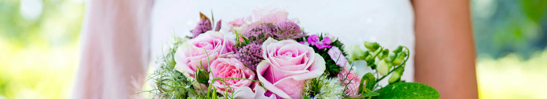 Hochzeit feiern im ATLANTIC Hotel Airport Bremen Braut hält einen üppigen Blumenstrauß mit rosa Rosen und grünen Akzenten vor einem verschwommenen, grünen Hintergrund.
