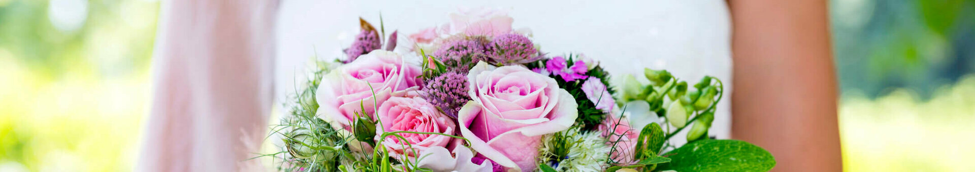 Bride holding a lush bouquet of pink roses with green accents against a blurred green background.