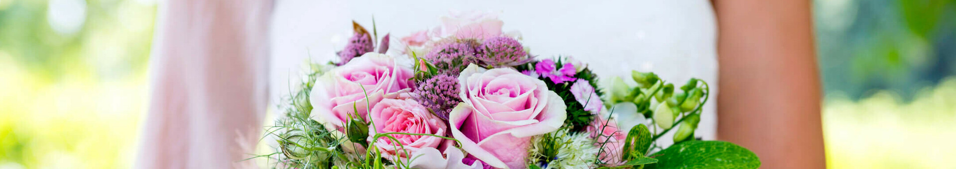 Hochzeit feiern im ATLANTIC Hotel Airport Bremen Braut hält einen üppigen Blumenstrauß mit rosa Rosen und grünen Akzenten vor einem verschwommenen, grünen Hintergrund.