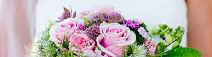 Hochzeit feiern im ATLANTIC Hotel Airport Bremen Braut hält einen üppigen Blumenstrauß mit rosa Rosen und grünen Akzenten vor einem verschwommenen, grünen Hintergrund.