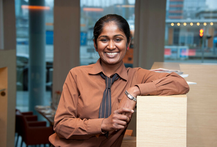 Eine lächelnde Hotelmitarbeiterin lehnt an einem Tresen im ATLANTIC Hotel Kiel.