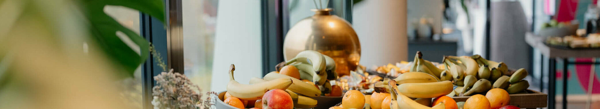 Frühstückstisch im ATLANTIC Hotel Münster mit frischen Früchten wie Bananen, Äpfeln und Passionsfrüchten.