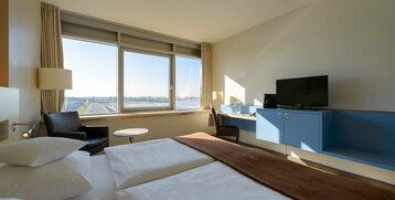Bright hotel room with double bed, view of the water, desk, TV and armchair by the window at the ATLANTIC Hotel Sail City.