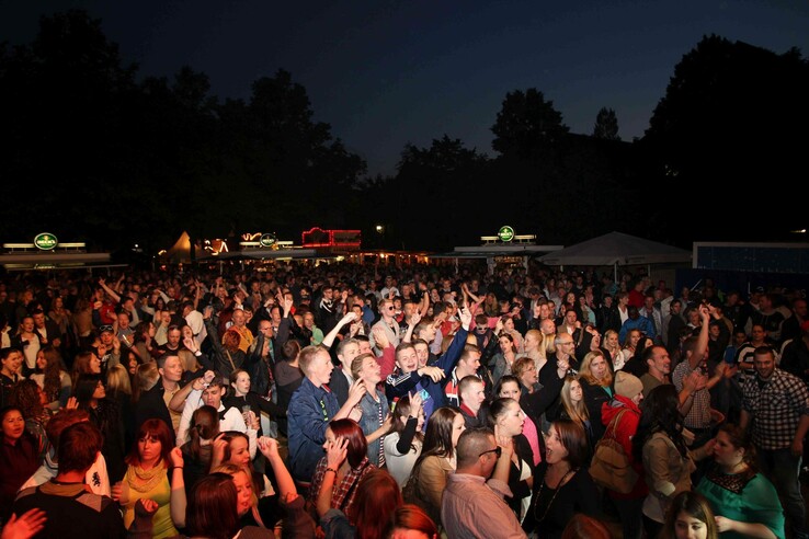 A large crowd celebrates at night on a floodlit festival site.