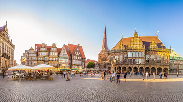 Historischer Marktplatz in Bremen mit Rathaus, Kirche und Menschen bei Sonnenschein.