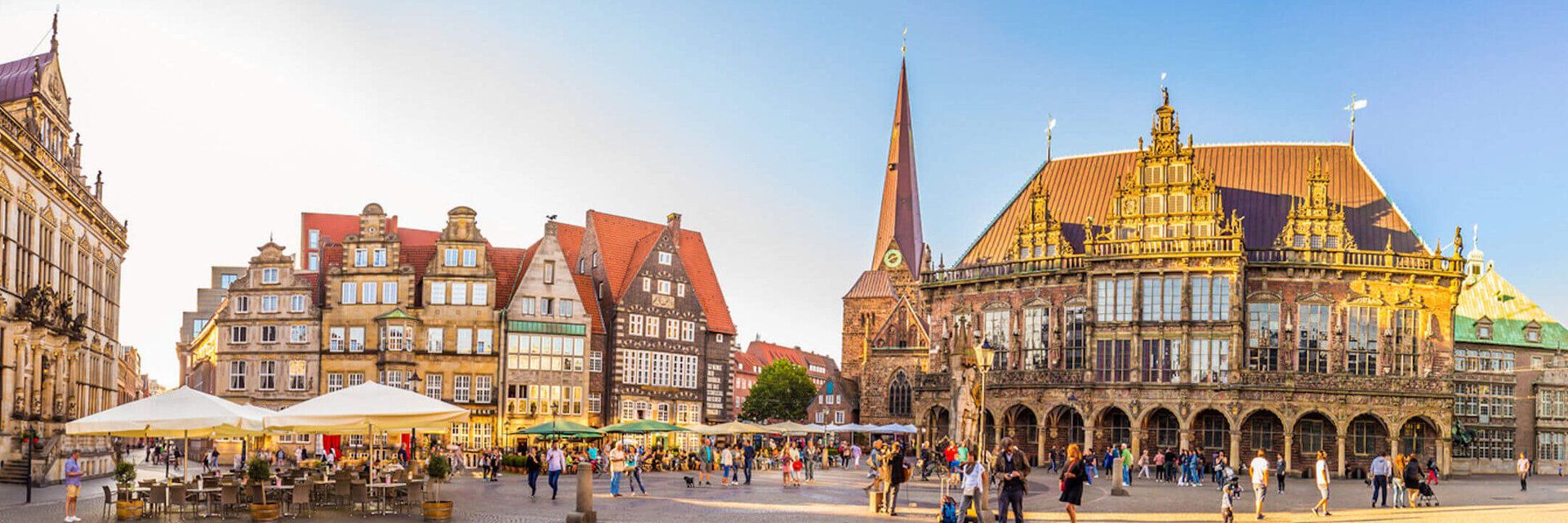 Historischer Marktplatz in Bremen mit Rathaus, Kirche und Menschen bei Sonnenschein.