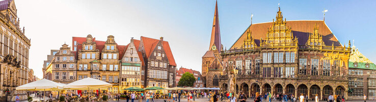 Historischer Marktplatz in Bremen mit Rathaus, Kirche und Menschen bei Sonnenschein.