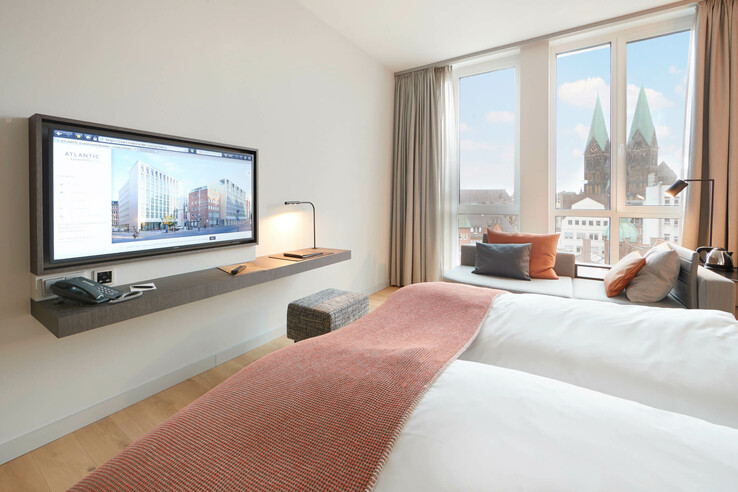 Helles Hotelzimmer mit Doppelbett, TV, Sofa und Blick auf den Bremer Dom durch große Fenster.