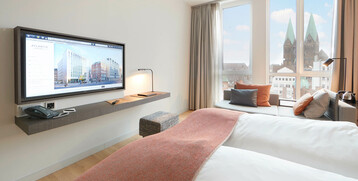 Helles Hotelzimmer mit Doppelbett, TV, Sofa und Blick auf den Bremer Dom durch große Fenster.