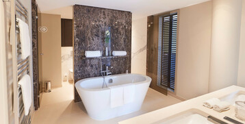 Modern bathroom with free-standing bathtub, towel rail, double washbasin and elegant marble wall in the ATLANTIC Grand Hotel Bremen.