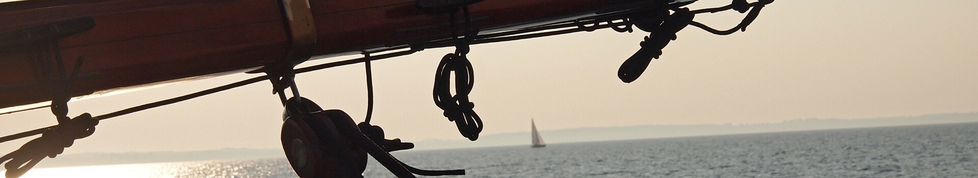 Segelboot auf ruhigem Meer bei Sonnenuntergang, mit Blick auf den Horizont und ein entferntes Segel.