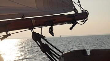 Sailboat on a calm sea at sunset, with a view of the horizon and a distant sail.