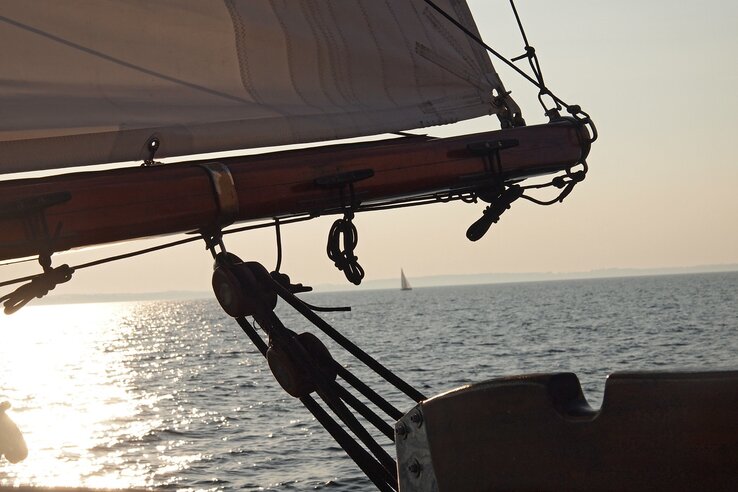 Segelboot auf ruhigem Meer bei Sonnenuntergang, mit Blick auf den Horizont und ein entferntes Segel.