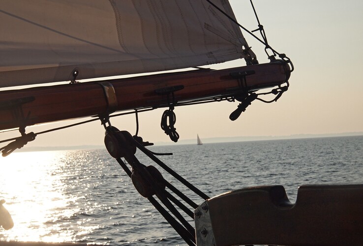 Segelboot auf ruhigem Meer bei Sonnenuntergang, mit Blick auf den Horizont und ein entferntes Segel.