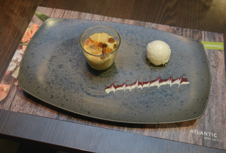 Dessert on a gray plate: cream in a glass, scoop of ice cream, decorative sauce. Hotel ATLANTIC Hotel Sail City, Bremerhaven.