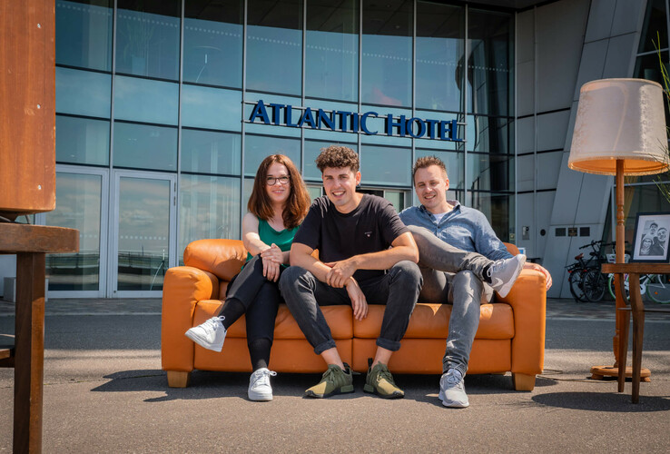 Drei Personen sitzen auf einem Sofa vor dem ATLANTIC Hotel Sail City in Bremerhaven.