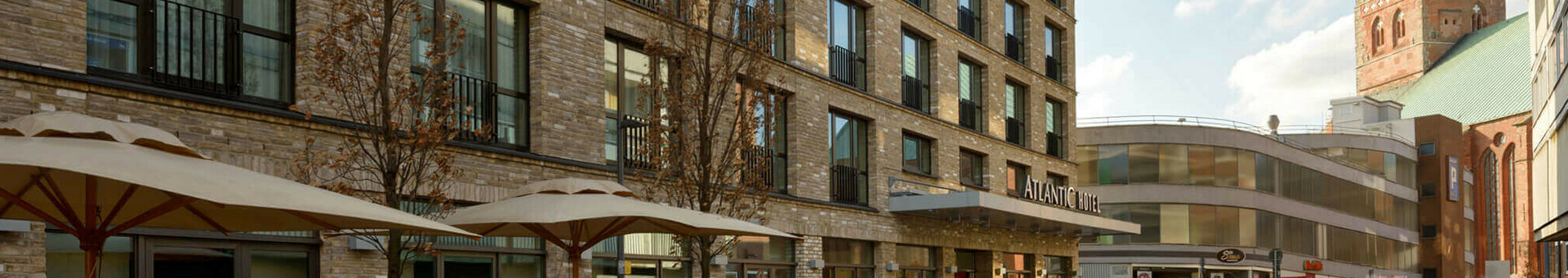 Facade of the ATLANTIC Hotel Lübeck with modern windows, sunshades and a church tower in the background.