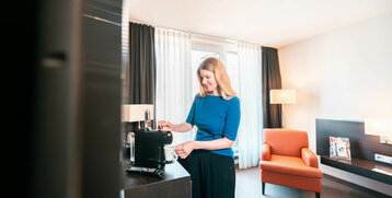 Frau macht sich einen Kaffee im Hotelzimmer des ATLANTIC Hotel Lübeck