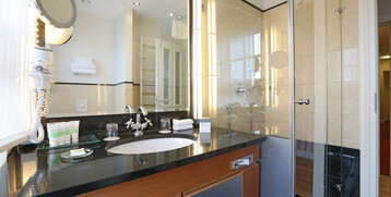 Modernes Badezimmer mit Glasdusche, Waschbecken, Spiegel und Pflegeprodukten im ATLANTIC Grand Hotel Travemünde.