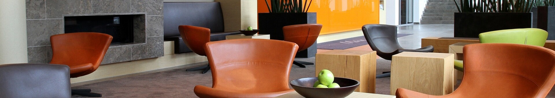 Modern hotel lobby with colorful armchairs, wooden tables, fireplace and reception in the background.