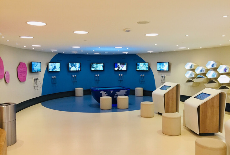 Modern, bright room with interactive screens, blue wall and seating in the Botanika Bremen.