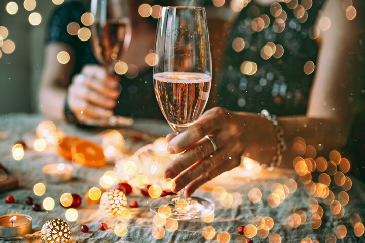 Weihnachtsfeiern l ATLANTIC Hotel Münster Zwei Personen stoßen mit Sektgläsern an, umgeben von stimmungsvoller Beleuchtung und Dekoration auf einem Tisch.