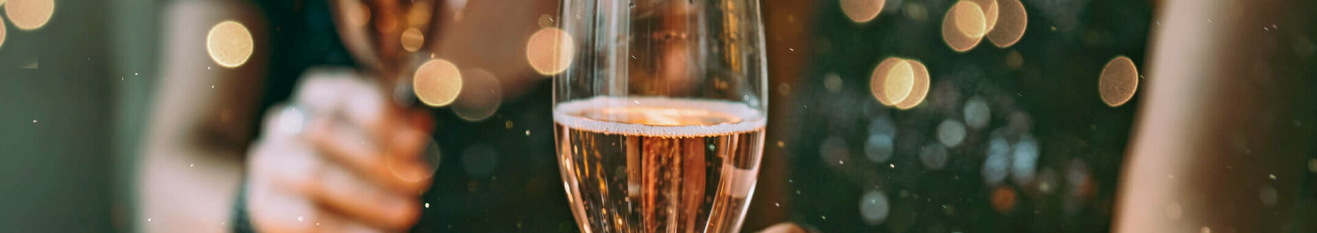 Christmas parties l ATLANTIC Hotel Münster Two people toast with champagne glasses, surrounded by atmospheric lighting and decorations on a table.
