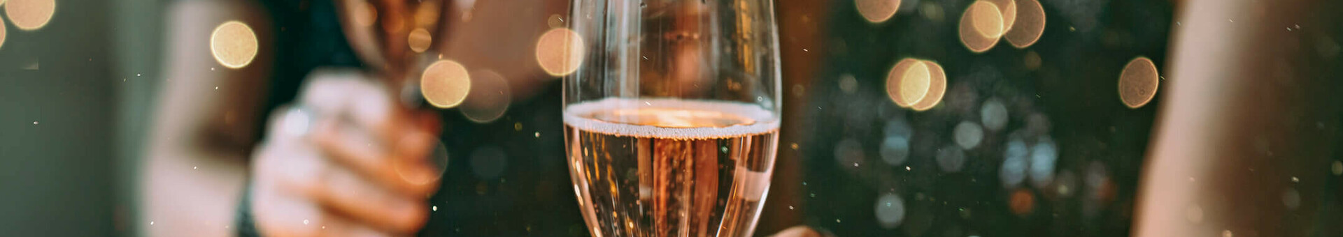 Weihnachtsfeiern l ATLANTIC Hotel Münster Zwei Personen stoßen mit Sektgläsern an, umgeben von stimmungsvoller Beleuchtung und Dekoration auf einem Tisch.