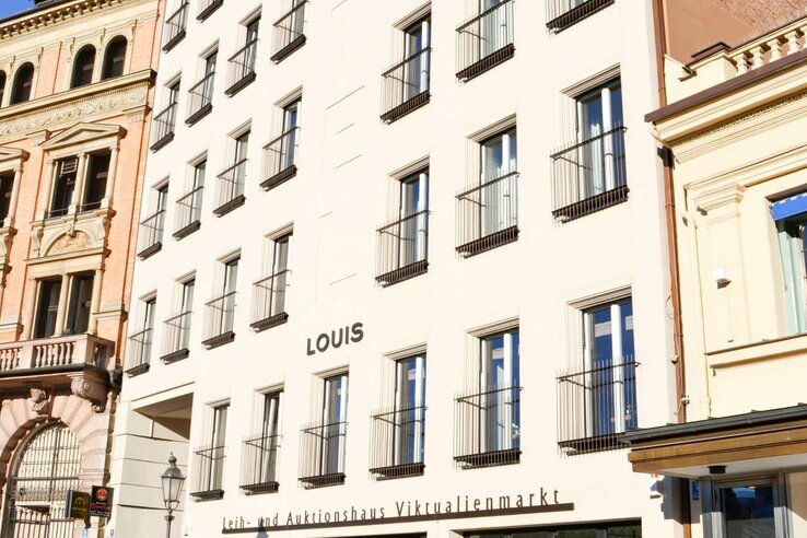 Façade of the LOUIS Hotel in Munich with several windows and a historic neighboring building.