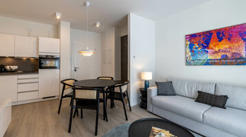 Modernes Hotelzimmer mit Küche, Esstisch, Sofa und bunter Wandkunst im ATLANTIC Grand Hotel Travemünde.