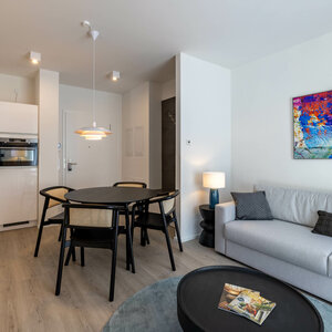 Living area in the flat category in the ATLANTIC Dependance | ATLANTIC Grand Hotel Travemünde Modern hotel room with kitchen, dining table, sofa and colorful wall art at the ATLANTIC Grand Hotel Travemünde.