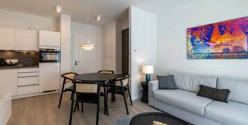 Modern hotel room with kitchen, dining table, sofa and colorful wall art at the ATLANTIC Grand Hotel Travemünde.