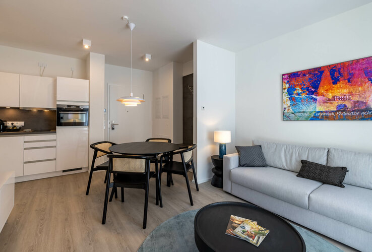 Modernes Hotelzimmer mit Küche, Esstisch, Sofa und bunter Wandkunst im ATLANTIC Grand Hotel Travemünde.