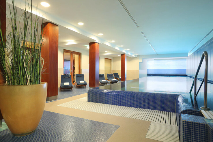 Heller Innenpoolbereich im ATLANTIC Grand Hotel Travemünde mit Liegestühlen und Pflanzen.