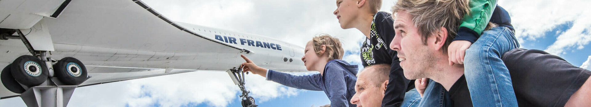 ATLANTIC Hotel Heidelberg Technik Museum Sinsheim  Family looking at airplane model outdoors, children on shoulders, blue sky in the background.