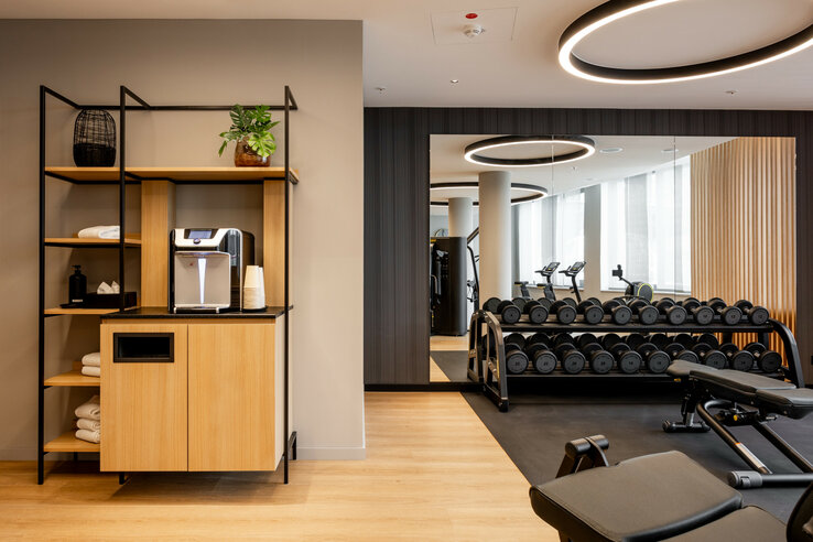 Moderner Fitnessraum im ATLANTIC Hotel Heidelberg mit Hanteln, Laufbändern und Erfrischungsstation.