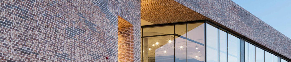 Brick building of the European Hanseatic Museum with illuminated entrance and large windows at dusk.