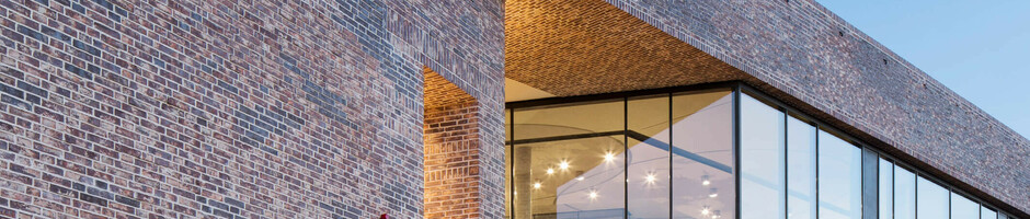 Backsteingebäude des Europäischen Hansemuseums mit beleuchtetem Eingang und großen Fenstern bei Abenddämmerung.