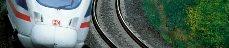 Ein moderner ICE-Zug fährt durch eine grüne, bewaldete Landschaft auf einer kurvigen Strecke.