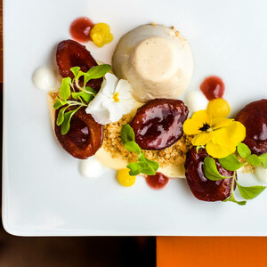 ATLANTIC Hotels Kochbuch Elegantes Dessert mit Panna Cotta, roten Früchten, essbaren Blüten und Kräutern auf weißem Teller.