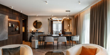 Elegantes Hotelzimmer mit modernem Essbereich, stilvollen Möbeln und großen Fenstern mit Vorhängen.