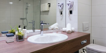 Modernes Hotelbad mit Waschbecken, Handtüchern, Pflegeprodukten und Glasdusche im ATLANTIC Hotel Landgut Horn Bremen.