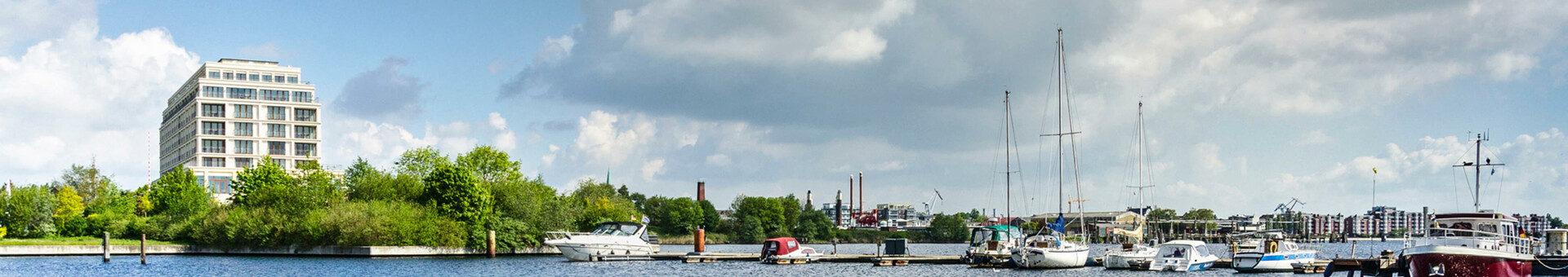 Hotel am Wasser mit Segelbooten im Vordergrund und blauem Himmel im Hintergrund.