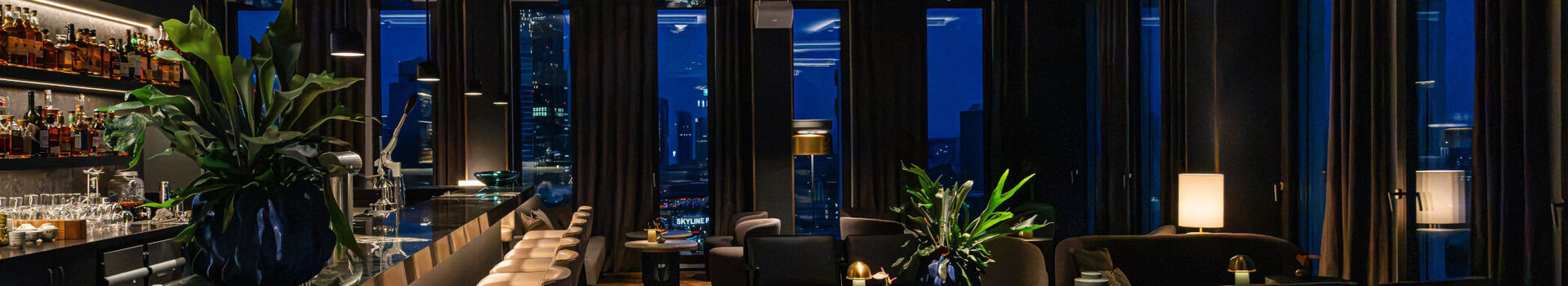 Moderne Bar mit stimmungsvollem Ambiente und dunklen Möbeln sowie Ausblick auf die Frankfurter Skyline.