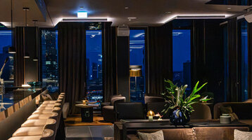 Moderne Bar mit stimmungsvollem Ambiente und dunklen Möbeln sowie Ausblick auf die Frankfurter Skyline.
