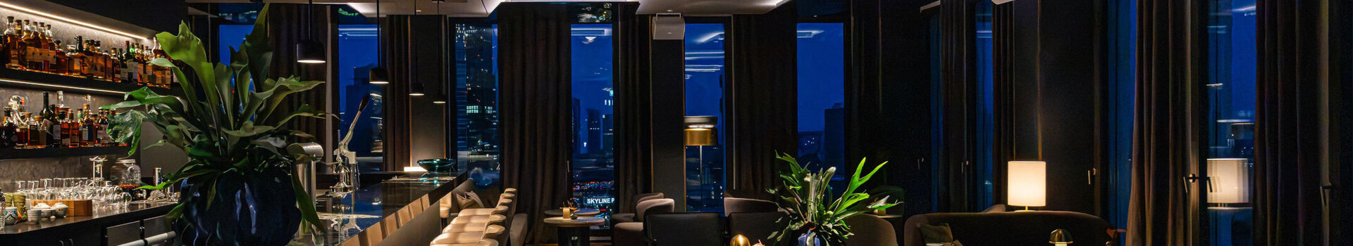 A modern bar with a cosy atmosphere, dark furniture and views of the Frankfurt skyline.