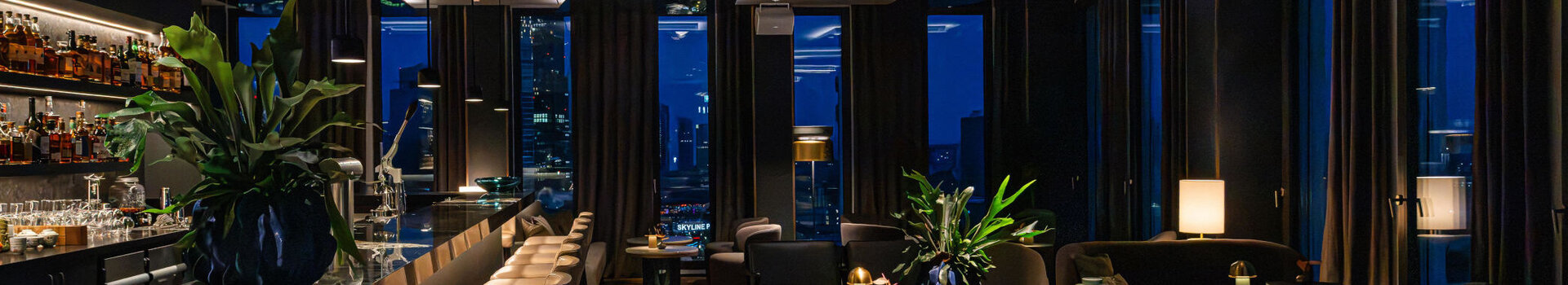 A modern bar with a cosy atmosphere, dark furniture and views of the Frankfurt skyline.
